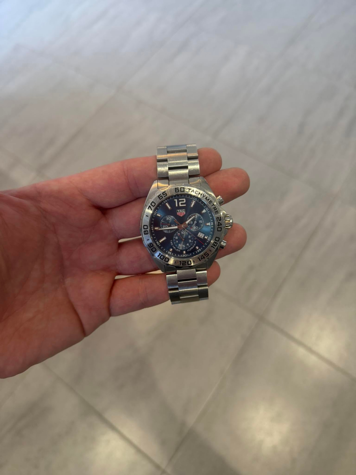 Steel chronograph watch with a dark dial held in one hand